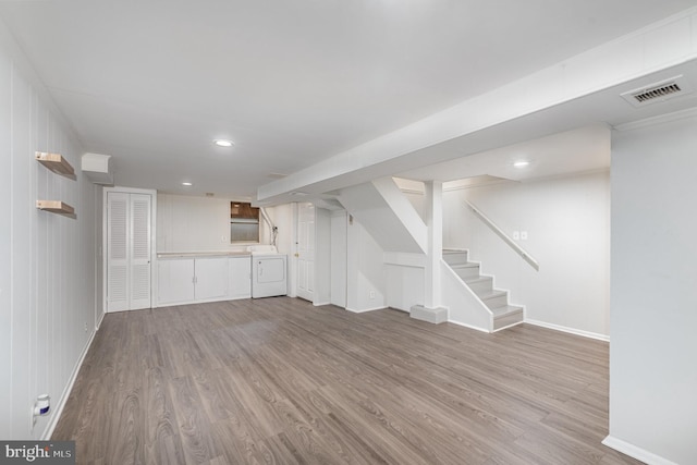 finished below grade area featuring washer / dryer, baseboards, visible vents, wood finished floors, and stairs