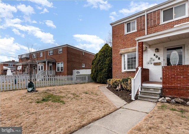 townhome / multi-family property with a porch, brick siding, and fence