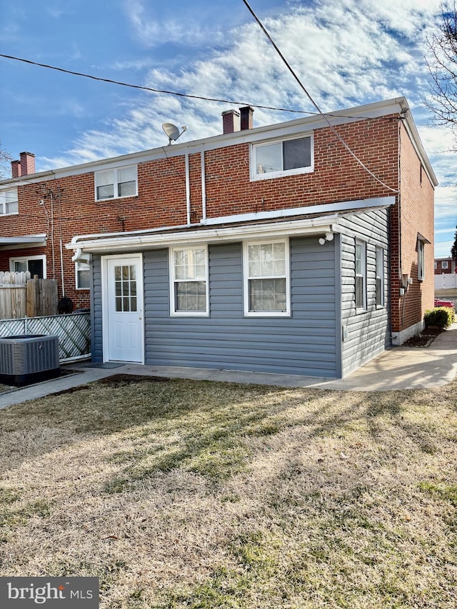 rear view of house featuring cooling unit, brick siding, fence, a lawn, and a chimney