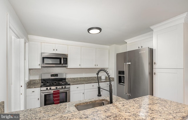 kitchen featuring appliances with stainless steel finishes, a sink, white cabinetry, and decorative backsplash