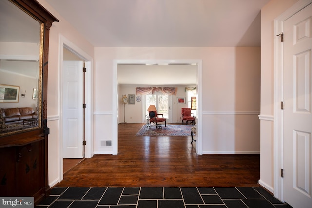 hall with dark wood-style floors, baseboards, and visible vents