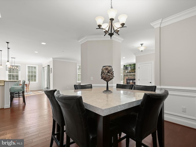 dining area with dark wood finished floors, a glass covered fireplace, an inviting chandelier, and ornamental molding