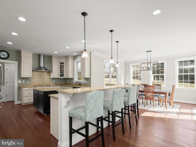 kitchen with dark wood-type flooring, a kitchen island, stainless steel gas stovetop, wall chimney range hood, and decorative backsplash