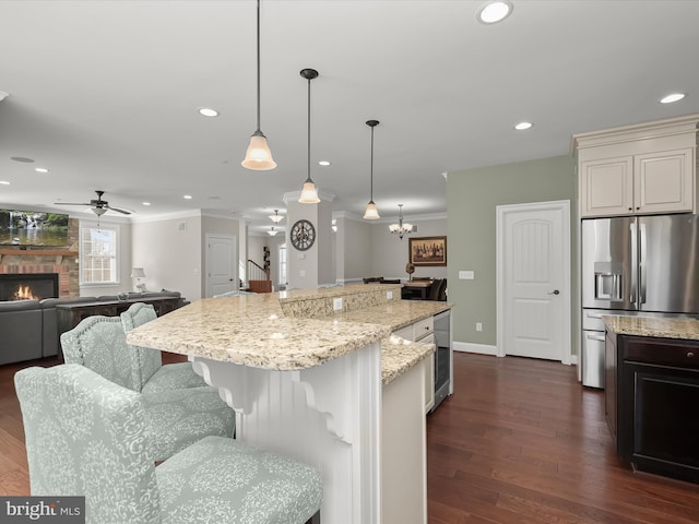 kitchen with dark wood-type flooring, a kitchen breakfast bar, a large fireplace, stainless steel fridge, and crown molding