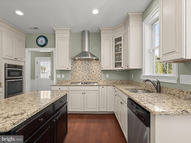 kitchen with visible vents, a sink, white cabinetry, stainless steel appliances, and wall chimney range hood