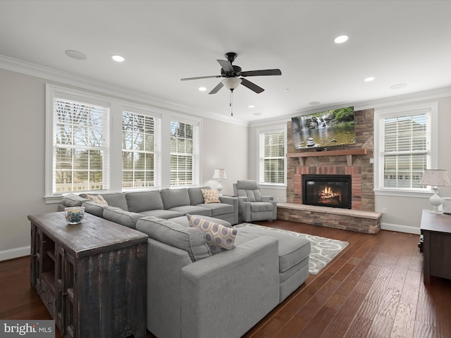 living room with a stone fireplace, crown molding, dark wood-style floors, and baseboards