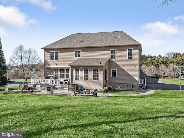 rear view of house featuring a patio area, a lawn, and roof with shingles