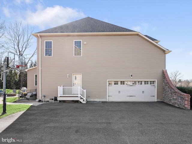 back of property featuring aphalt driveway, an attached garage, and a shingled roof