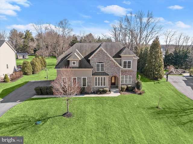 view of front of house featuring aphalt driveway, stone siding, roof with shingles, and a front yard