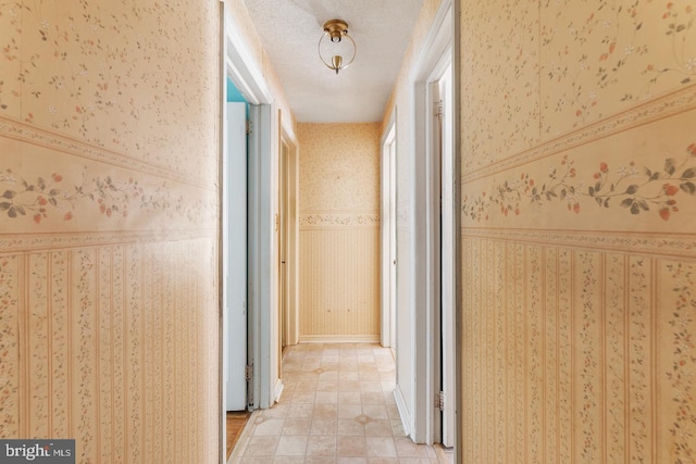 hallway with a textured ceiling, baseboards, and wallpapered walls