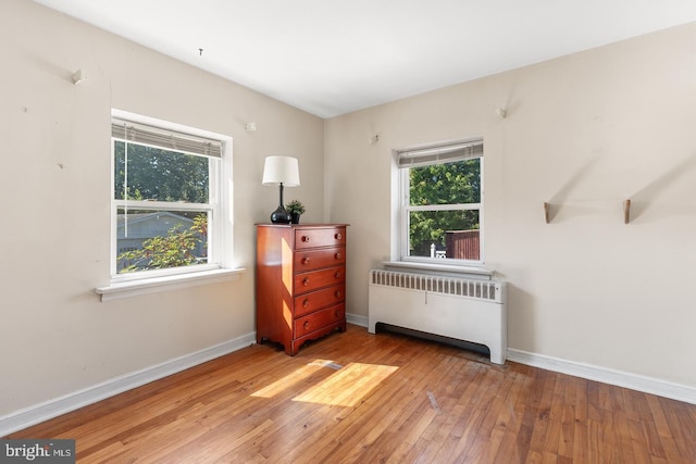 bedroom featuring radiator, multiple windows, wood-type flooring, and baseboards