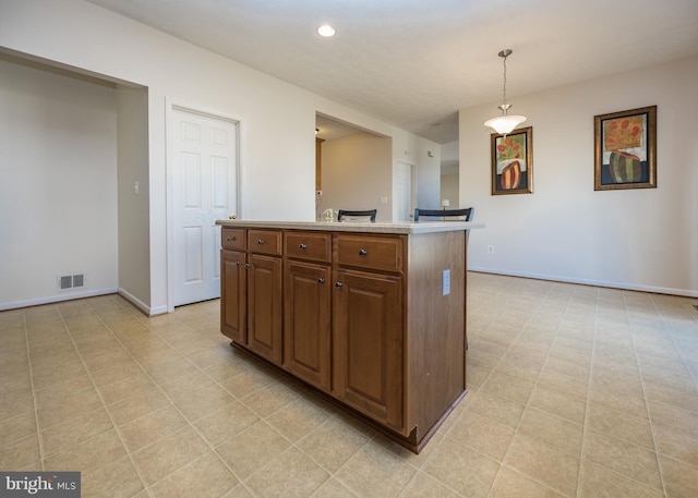 kitchen with baseboards, visible vents, decorative light fixtures, a kitchen island with sink, and light countertops