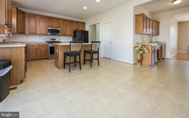 kitchen with appliances with stainless steel finishes, brown cabinetry, a sink, and light countertops