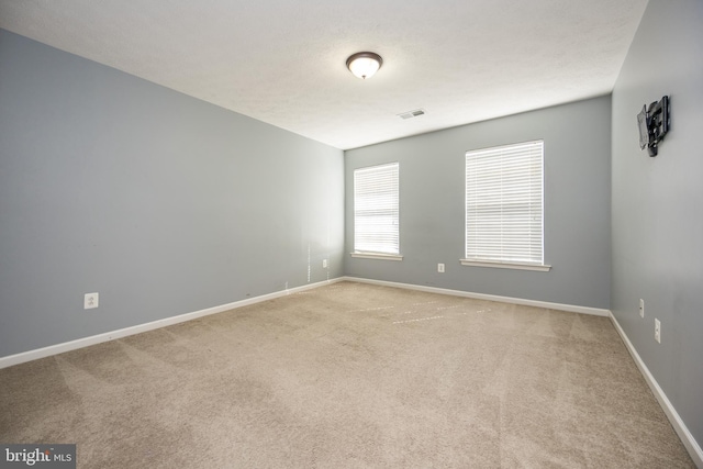 spare room with light colored carpet, visible vents, and baseboards