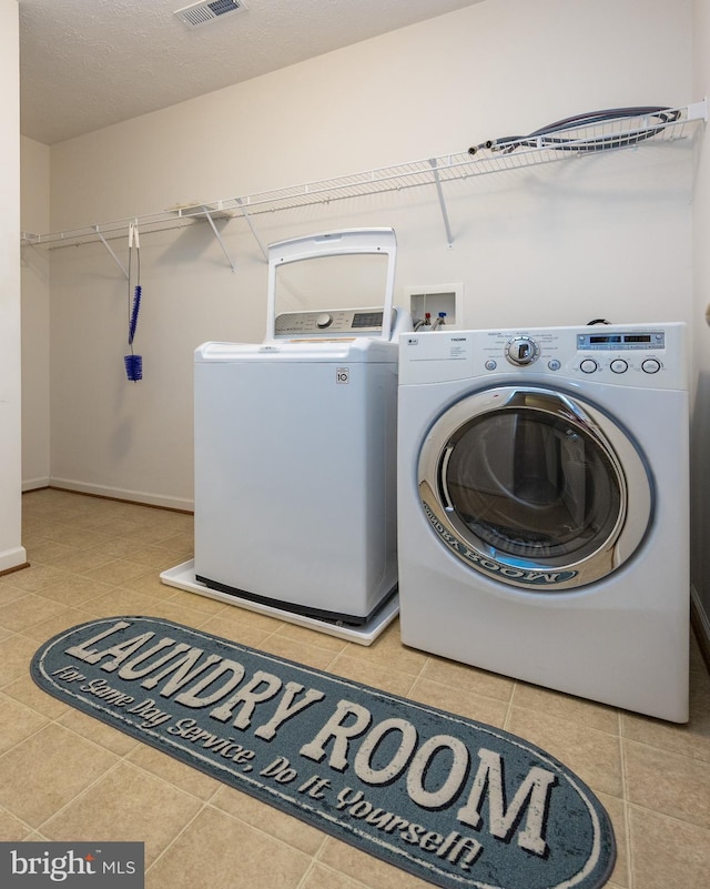 clothes washing area featuring washing machine and dryer, laundry area, visible vents, and light tile patterned floors