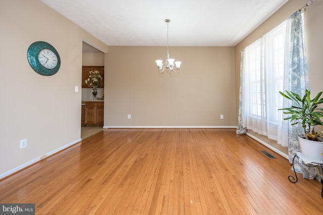 unfurnished room with light wood-type flooring, visible vents, a notable chandelier, and baseboards