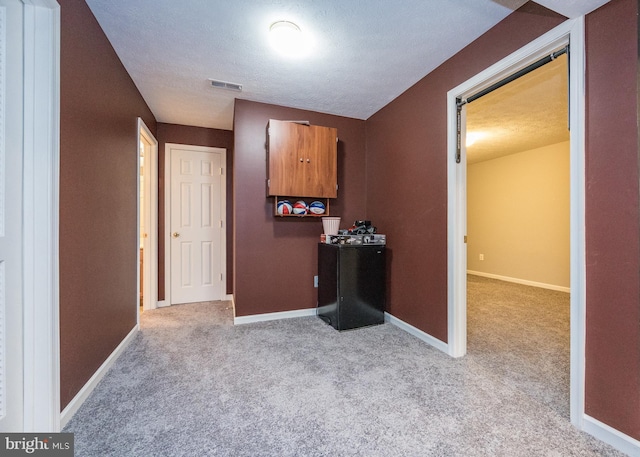 corridor featuring a textured ceiling, carpet, visible vents, and baseboards