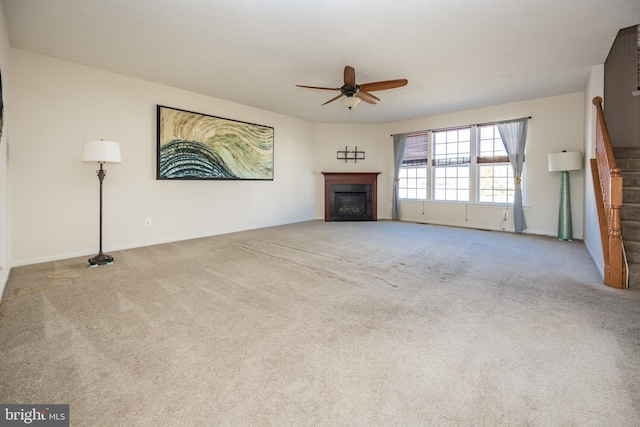 unfurnished living room with stairs, carpet floors, a glass covered fireplace, and a ceiling fan