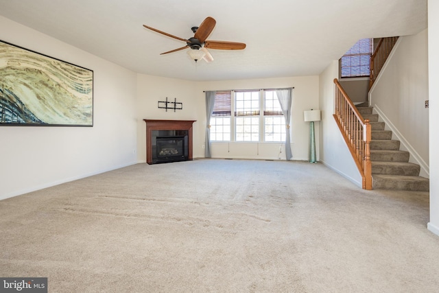 unfurnished living room with baseboards, a glass covered fireplace, ceiling fan, carpet, and stairs