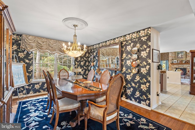 dining area featuring a notable chandelier, a large fireplace, wood finished floors, baseboards, and wallpapered walls