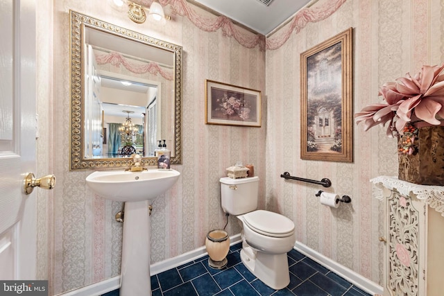 bathroom featuring toilet, a sink, baseboards, tile patterned floors, and wallpapered walls