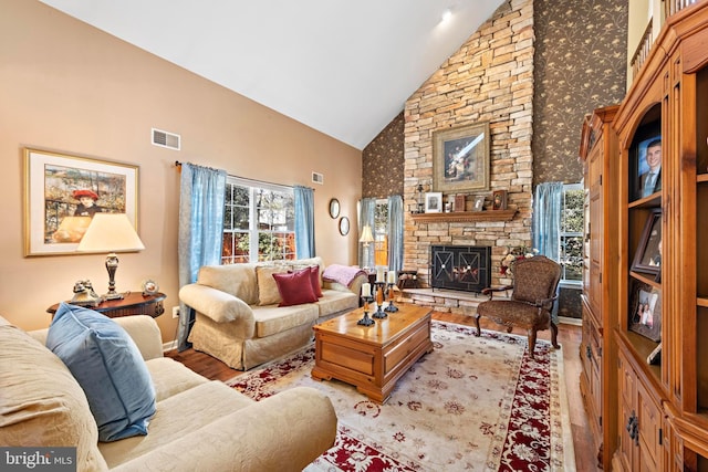 living area with high vaulted ceiling, a stone fireplace, visible vents, and light wood-style floors