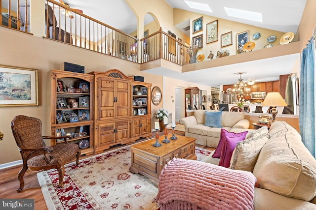 living room featuring a skylight, a notable chandelier, wood finished floors, high vaulted ceiling, and baseboards