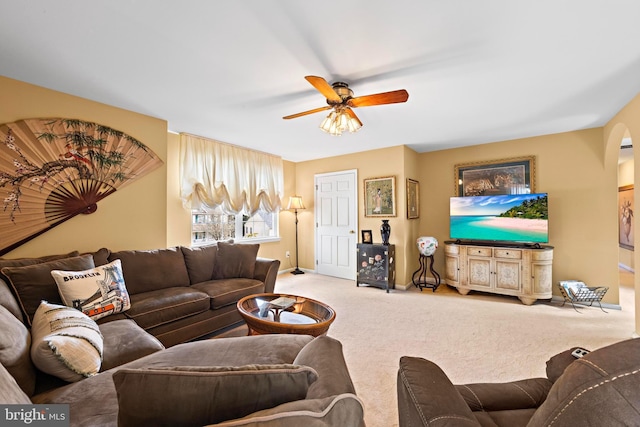 carpeted living area with arched walkways, a ceiling fan, and baseboards