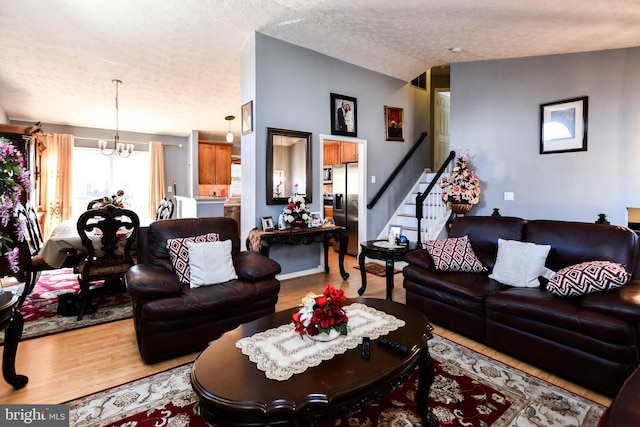 living room with a chandelier, stairs, vaulted ceiling, wood finished floors, and a textured ceiling