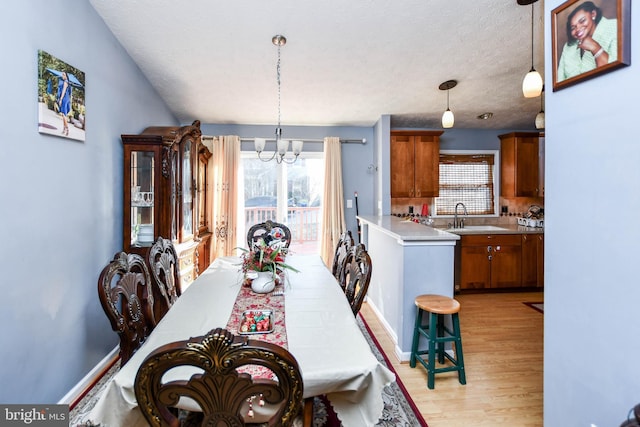 dining area featuring a notable chandelier, baseboards, light wood-type flooring, and a textured ceiling