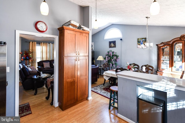 kitchen with hanging light fixtures, vaulted ceiling, light wood-type flooring, and a textured ceiling