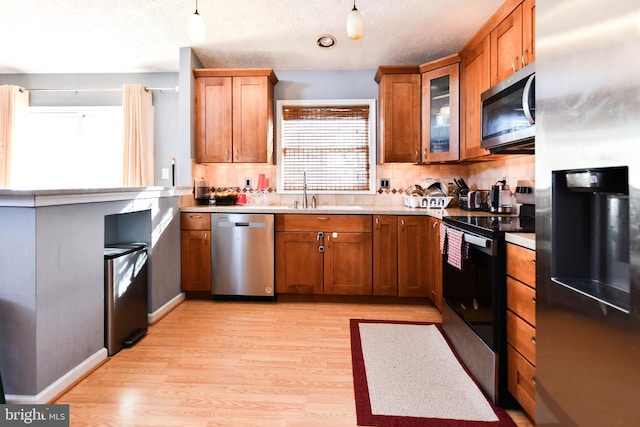 kitchen featuring backsplash, light wood-type flooring, brown cabinets, appliances with stainless steel finishes, and a sink