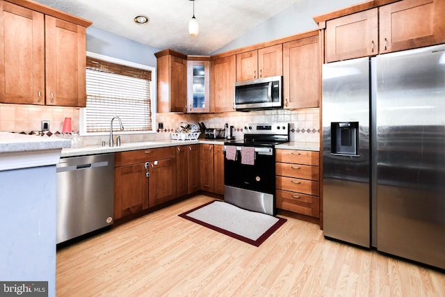 kitchen with a sink, light wood-style floors, appliances with stainless steel finishes, glass insert cabinets, and lofted ceiling