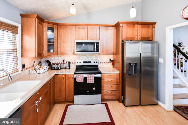 kitchen featuring a sink, stainless steel appliances, lofted ceiling, and light wood finished floors