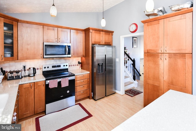 kitchen featuring hanging light fixtures, lofted ceiling, light wood-style flooring, and appliances with stainless steel finishes