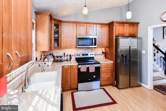 kitchen with brown cabinets, lofted ceiling, a sink, stainless steel appliances, and light wood-type flooring