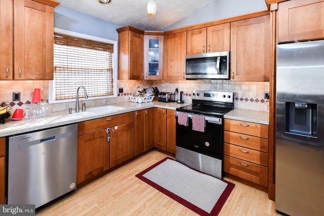 kitchen with lofted ceiling, light wood-type flooring, appliances with stainless steel finishes, and a sink