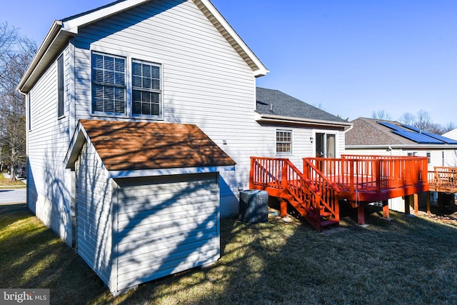 back of house featuring a lawn, a deck, and roof with shingles