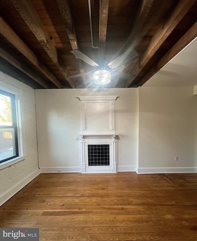 unfurnished living room featuring beamed ceiling, a tiled fireplace, wood finished floors, and baseboards