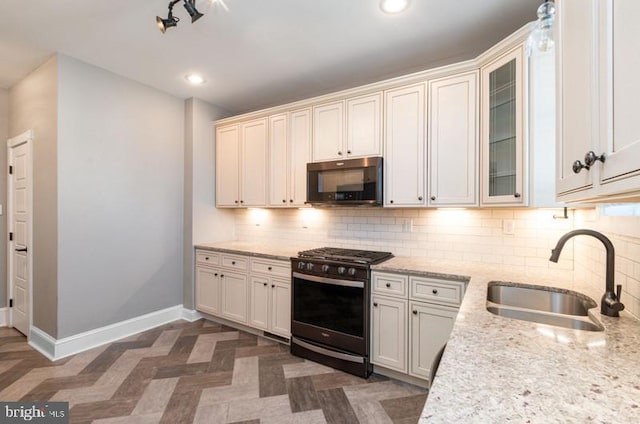 kitchen featuring stainless steel range with gas cooktop, backsplash, a sink, and baseboards