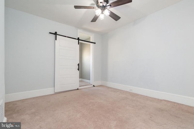 carpeted spare room featuring a barn door, baseboards, and a ceiling fan