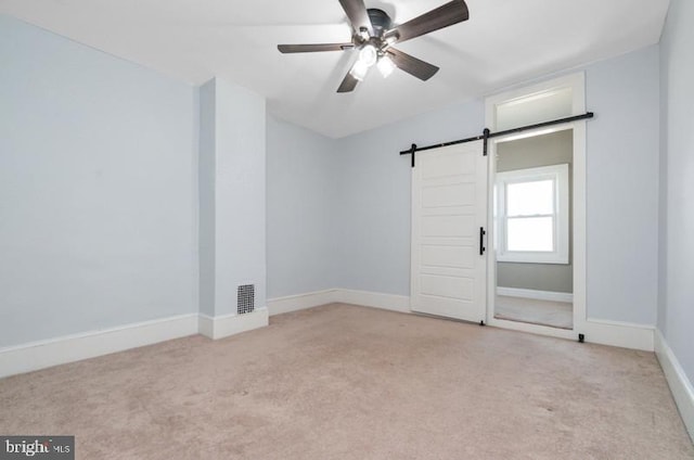 spare room with a ceiling fan, carpet, visible vents, and a barn door