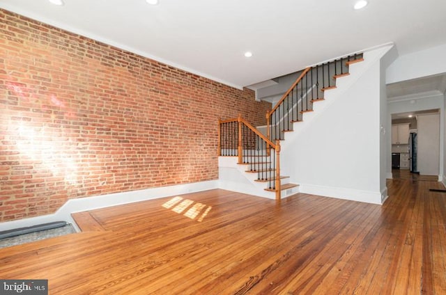 unfurnished living room with stairs, recessed lighting, brick wall, baseboards, and hardwood / wood-style flooring