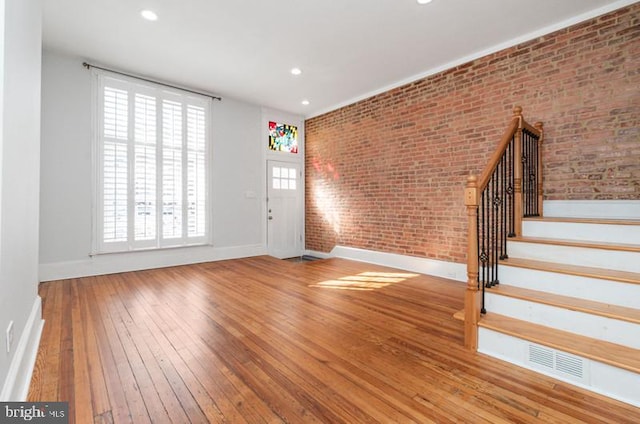 entryway featuring baseboards, visible vents, brick wall, wood-type flooring, and stairs