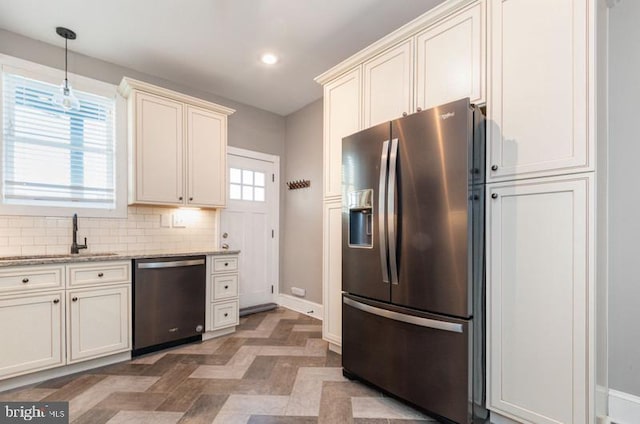 kitchen with stainless steel appliances, a sink, baseboards, light stone countertops, and tasteful backsplash