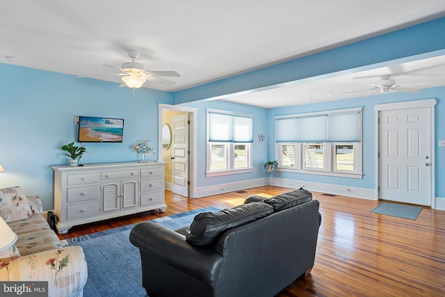 living room featuring visible vents, baseboards, wood finished floors, and a ceiling fan