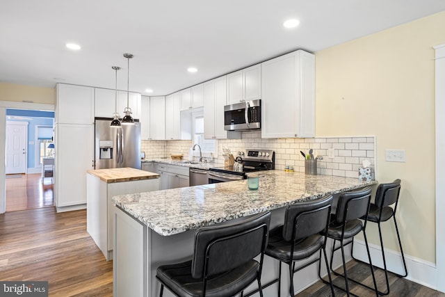 kitchen with a kitchen island, dark wood finished floors, a peninsula, stainless steel appliances, and butcher block counters