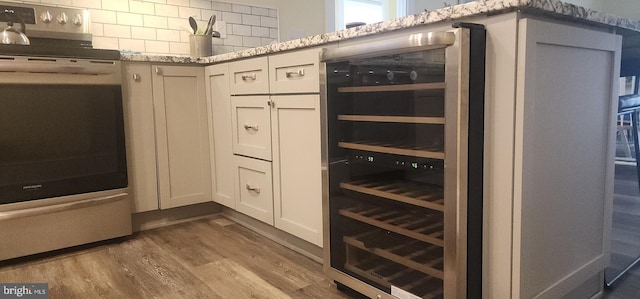 kitchen with wood finished floors, stainless steel range with electric cooktop, wine cooler, decorative backsplash, and light stone countertops