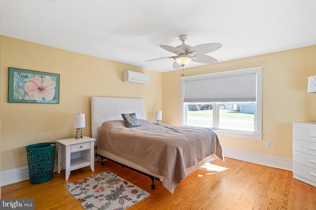 bedroom featuring baseboards, light wood-style floors, a ceiling fan, and a wall mounted AC