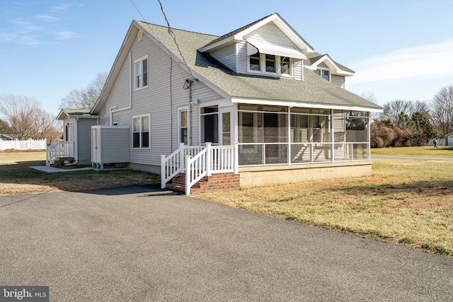 view of front of home featuring roof with shingles, a front yard, and a sunroom